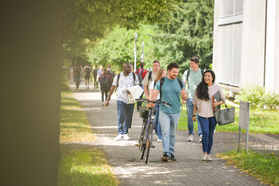 Gruppe junger Studierender gehen gemeinsam bei sonnigem Wetter über den Campus und unterhalten sich.