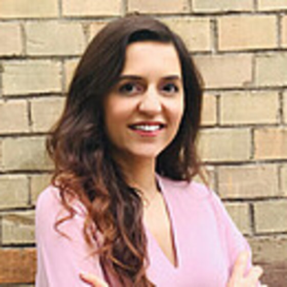 Foto: Eine Gruppe von Personen sitzt in einem Hörsaal und hört einem Vortrag zu. Im Vordergrund ist eine Person mit einem Laptop zu sehen. Der Raum ist mit Tischen und Stühlen ausgestattet.