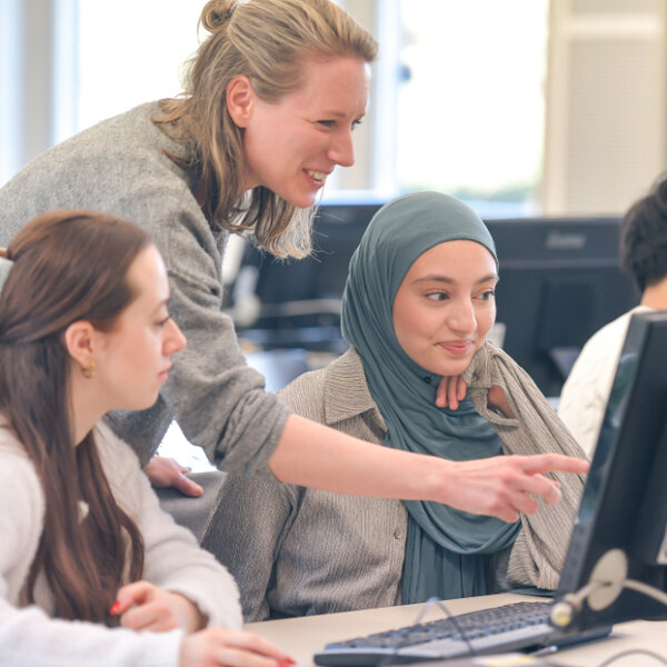 Lehrende zeigt drei Studierenden etwas am Bildschirm in einem Computerraum.