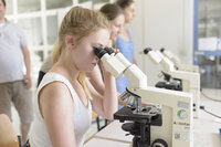 Foto: Mehrere Personen in einem Labor nutzen Mikroskope. Ein Mikroskop ist mit 'Axiostar plus' beschriftet. Die Umgebung wirkt akademisch.