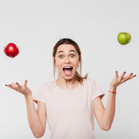 Foto: Eine Person in einem hellen T-Shirt jongliert mit einem roten und einem grünen Apfel vor einem neutralen Hintergrund. Die Arme sind seitlich ausgestreckt, während die Äpfel in der Luft schweben.