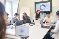 Gruppe von Studierenden diskutiert an einem Konferenztisch mit Laptops.