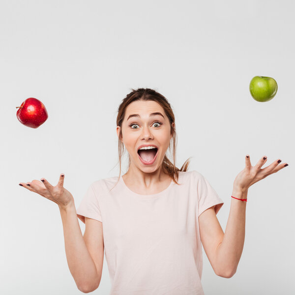 Foto: Eine Person in einem hellen T-Shirt jongliert mit einem roten und einem grünen Apfel vor einem neutralen Hintergrund. Die Arme sind seitlich ausgestreckt, während die Äpfel in der Luft schweben.