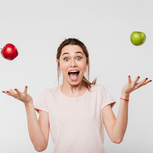 Foto: Eine Person in einem hellen T-Shirt jongliert mit einem roten und einem grünen Apfel vor einem neutralen Hintergrund. Die Arme sind seitlich ausgestreckt, während die Äpfel in der Luft schweben.
