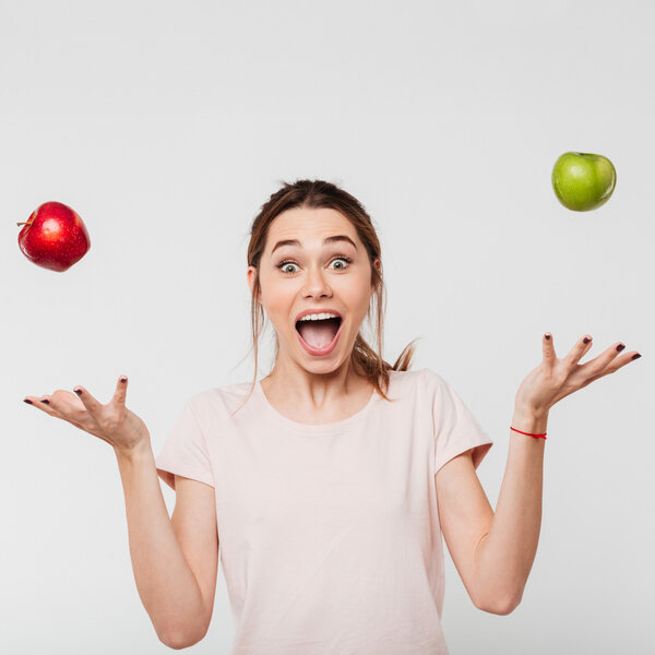 Foto: Eine Person in einem hellen T-Shirt jongliert mit einem roten und einem grünen Apfel vor einem neutralen Hintergrund. Die Arme sind seitlich ausgestreckt, während die Äpfel in der Luft schweben.