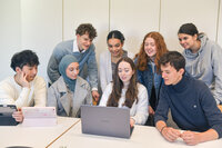 Foto: Eine Gruppe von Personen sitzt und steht um einen Tisch. Sie verwenden Laptops und Tablets. Die Personen sind in einem Raum mit weißen Wänden und tragen verschiedene Freizeitkleidung. Ein Laptop auf dem Tisch hat das Huawei-Logo.