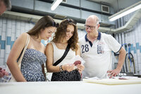 Foto: Drei Personen stehen in einem Labor und betrachten eine Fleischprobe. Eine Person hält die Probe in der Hand. Im Hintergrund sind Laborgeräte und Kacheln sichtbar.