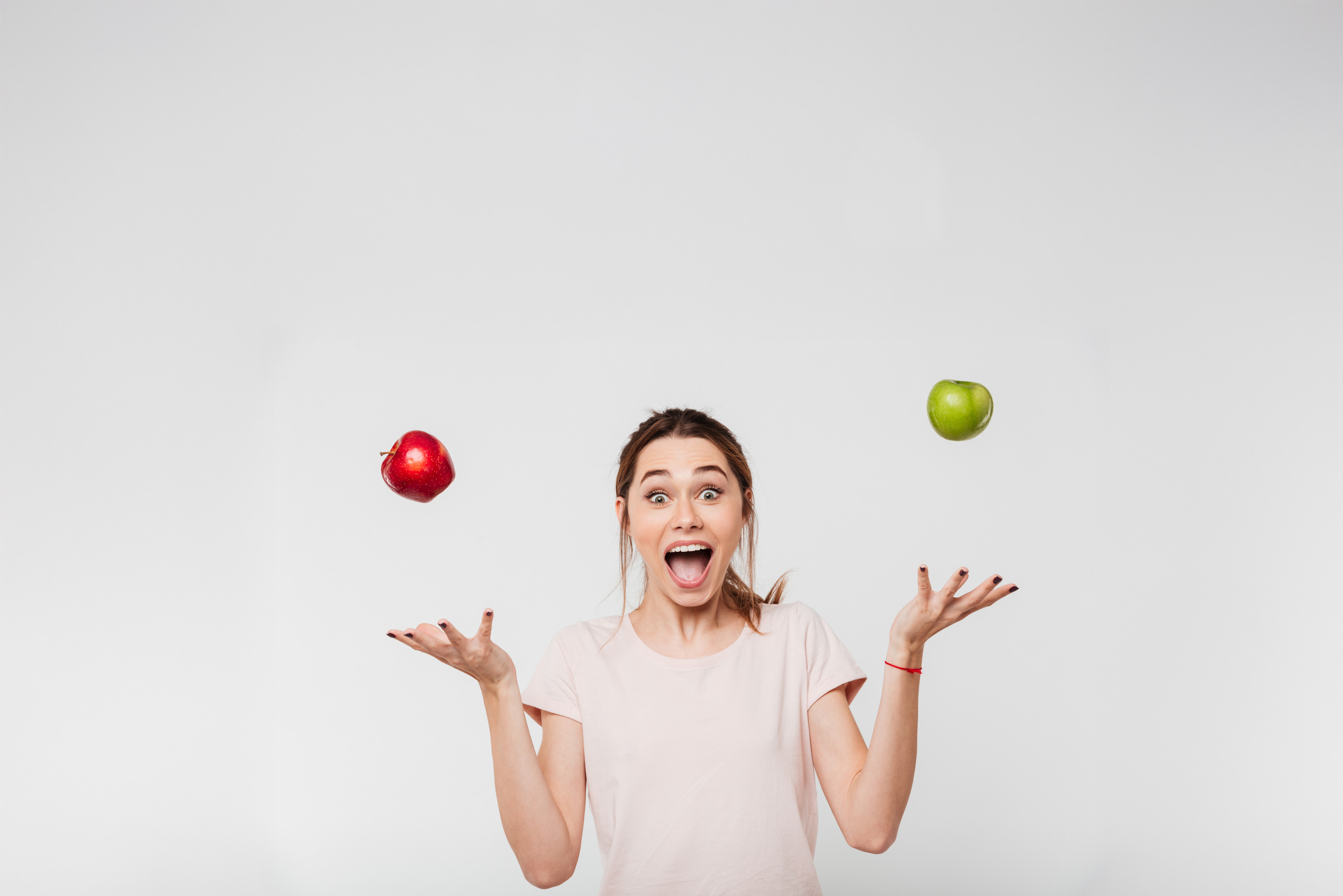 Foto: Eine Person in einem hellen T-Shirt jongliert mit einem roten und einem grünen Apfel vor einem neutralen Hintergrund. Die Arme sind seitlich ausgestreckt, während die Äpfel in der Luft schweben.